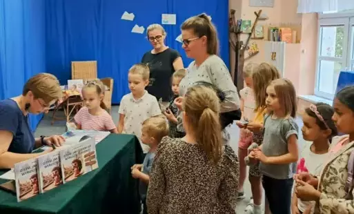 Nauczycielka wpisuje dedykację dla dzieci w swojej książce